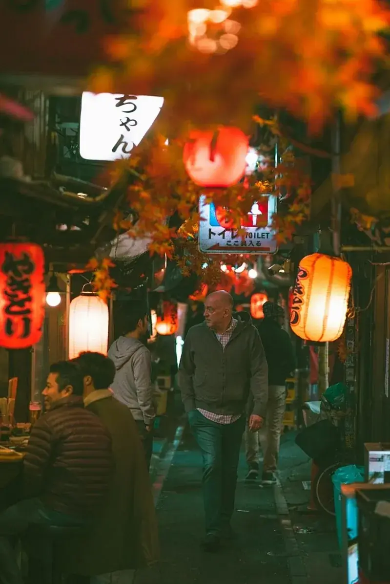 A narrow lantern-lit street at night in a Japanese old town, with signs and people walking.