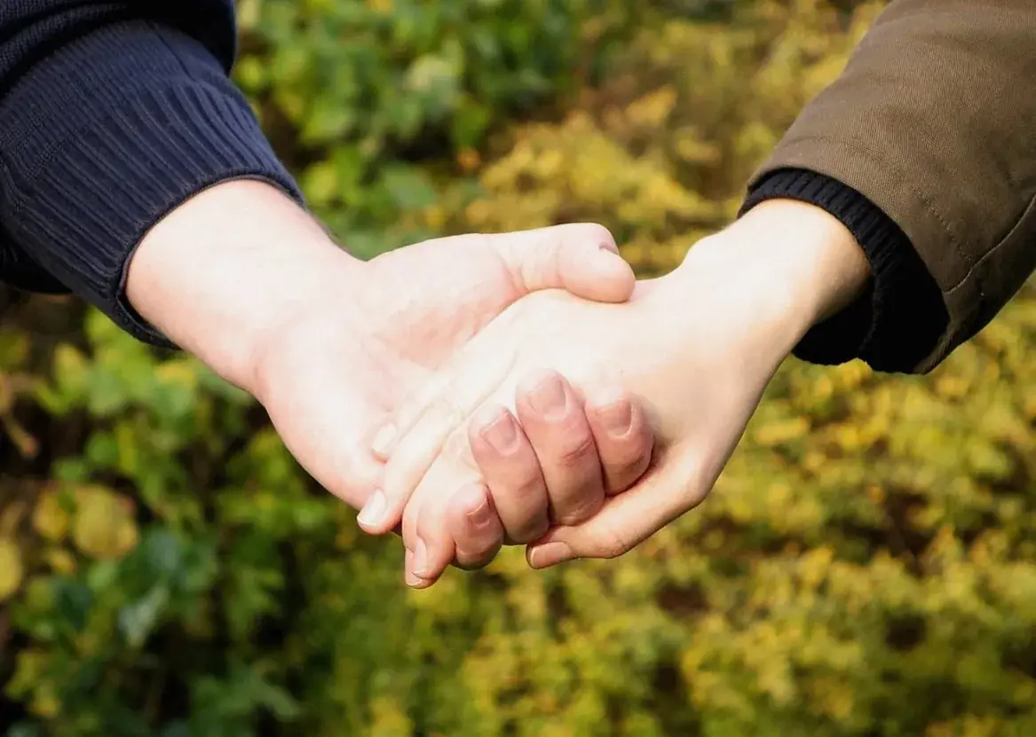 Two hands clasped together in front of blurred green foliage.