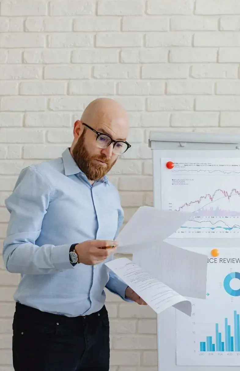 A man in a blue shirt holding printed charts beside a wall of diagrams.