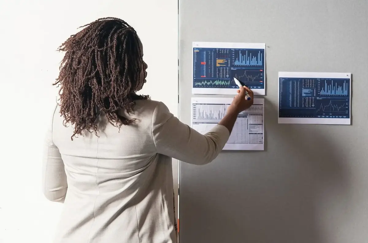 A woman pointing at printed charts pinned to a wall.